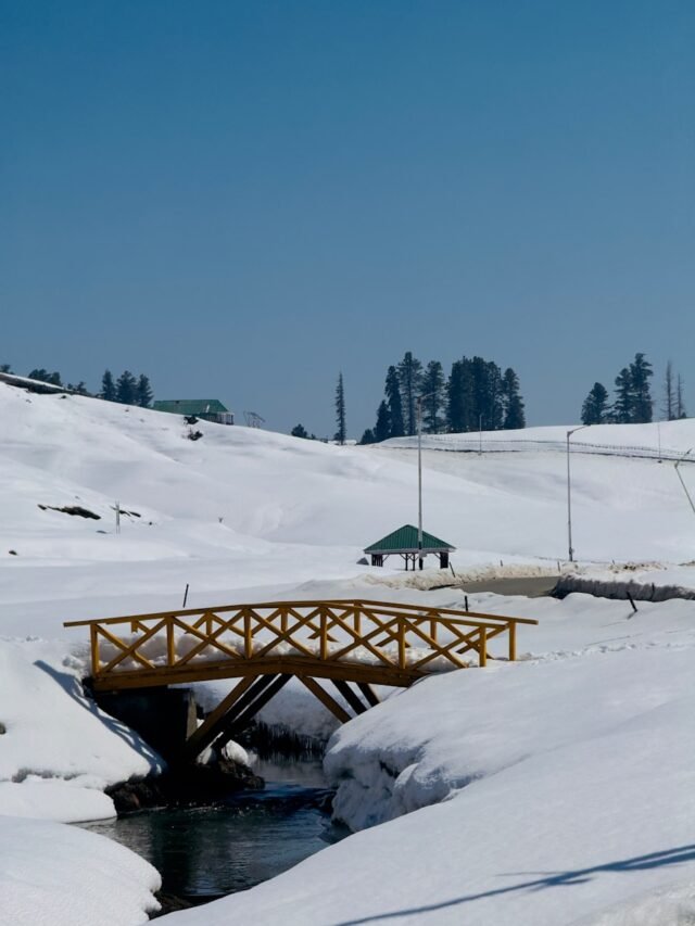 Snow-covered landscape with a wooden bridge and water in gulmarg